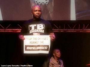 TAC Secretary General holds a sign demanding charges be dropped against 117 community health workers, activists who protested outside the Free State health department last year.