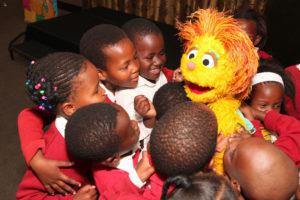 Learners from Shad Mashologu Junior Primary School playing with a muppet from Takalani Sesame TV show